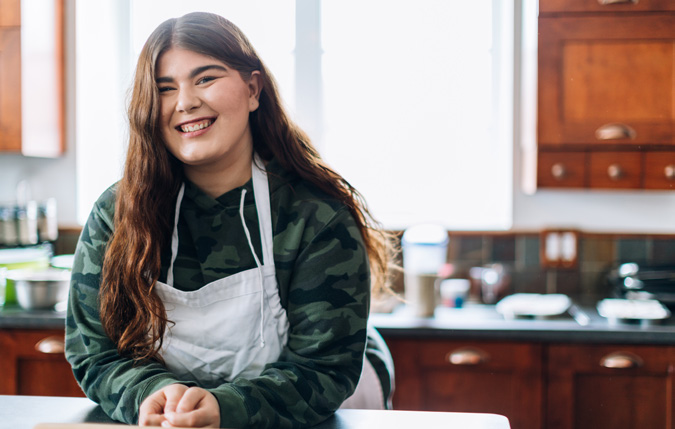 Woman smiling in a kitchen wearing an apron.