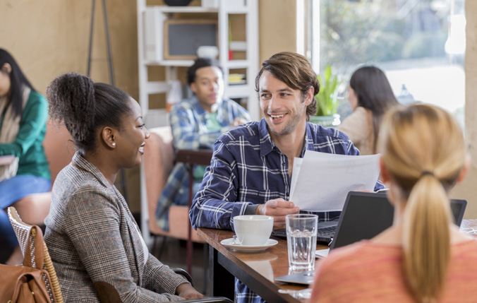 Group of people sitting around a table having coffee and smiling